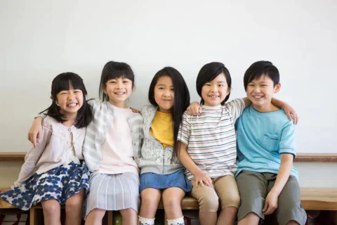 5人の児童が肩を組んで室内のベンチに座っている写真